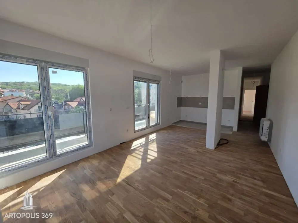 Empty living room with hardwood flooring and large windows overlooking the neighborhood.