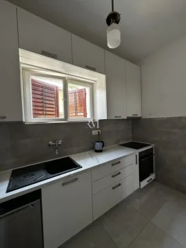 Modern white kitchen with a sink, built-in cooktop, and a window with shutters. - image 2
