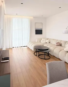 Living room with a comfortable beige sofa, wooden flooring, and a large window. - image 14