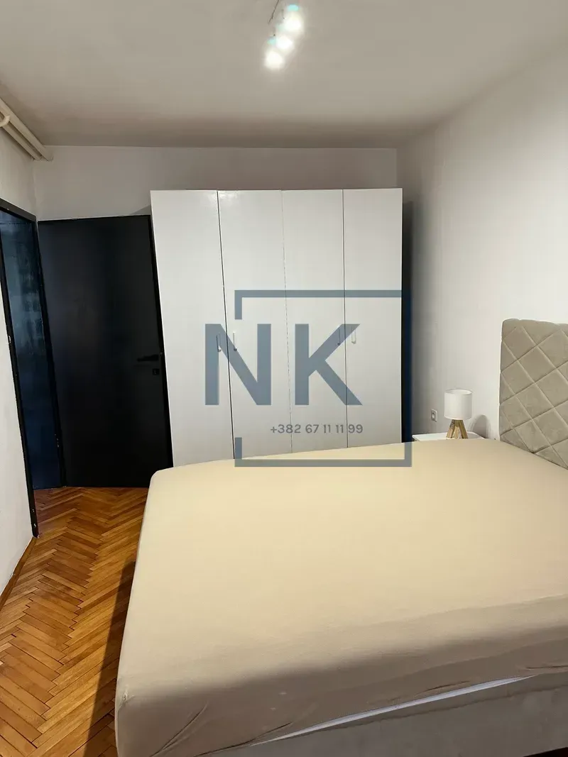 Furnished bedroom with a double bed, white wardrobe, and wooden parquet flooring.