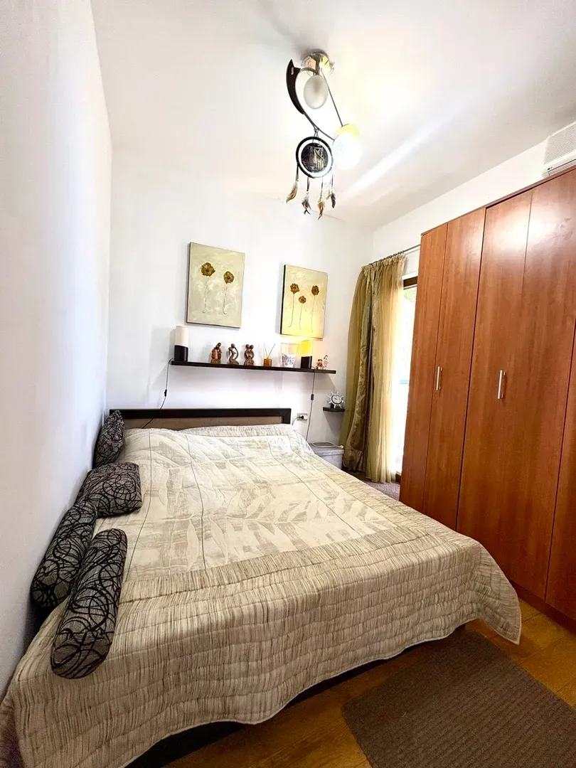 Spavaća soba sa bračnim krevetom, drvenim ormarom i ukrasnim detaljima na zidu.