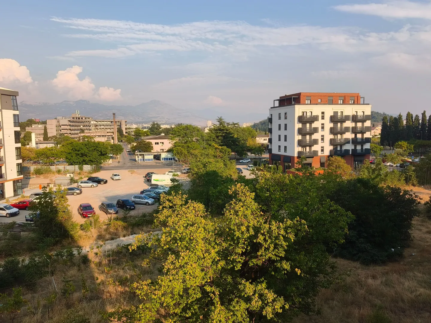 View from the window showing surrounding buildings, greenery, and mountains in the distance.