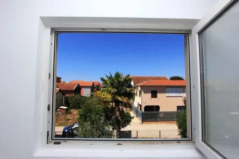 Pogled kroz otvoren prozor na okolne kuće i palmu. - image 13