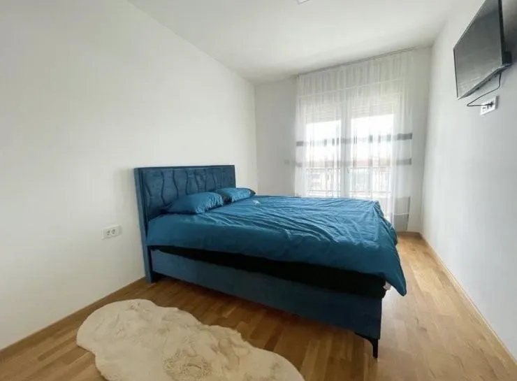 Spavaća soba sa bračnim krevetom, drvenim podom i televizorom na zidu.