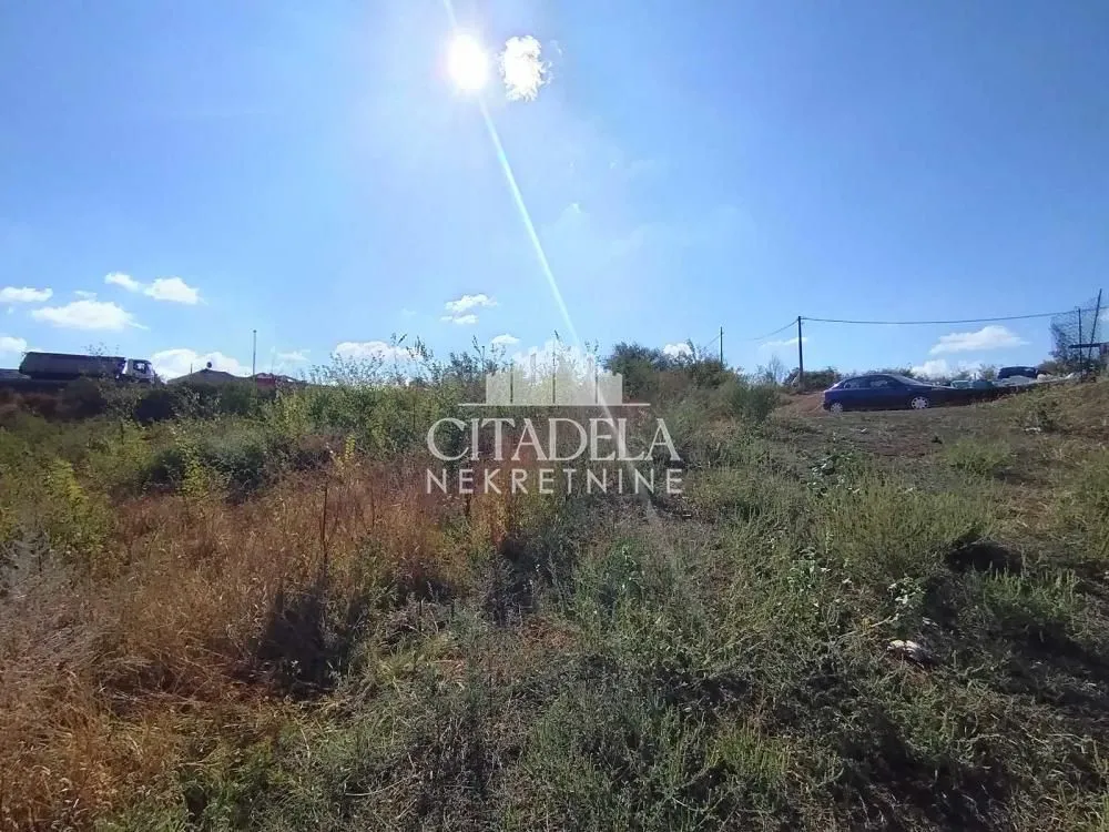 Pogled na neuuređeni plac sa rastinjem i vedrim nebom.