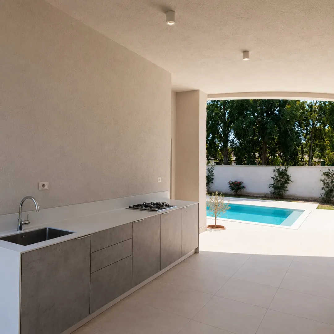 Covered patio area with an outdoor kitchen and a view of the swimming pool.