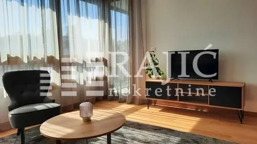 Living room with furniture, television, and large windows with light curtains.