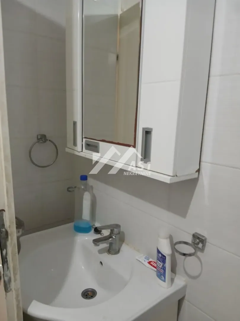 Manje kupatilo sa umivaonikom i ormarićem sa ogledalom na zidu.