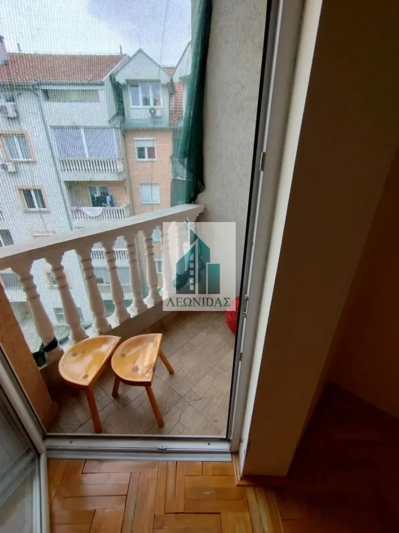Small balcony overlooking neighbouring buildings with wooden stools.