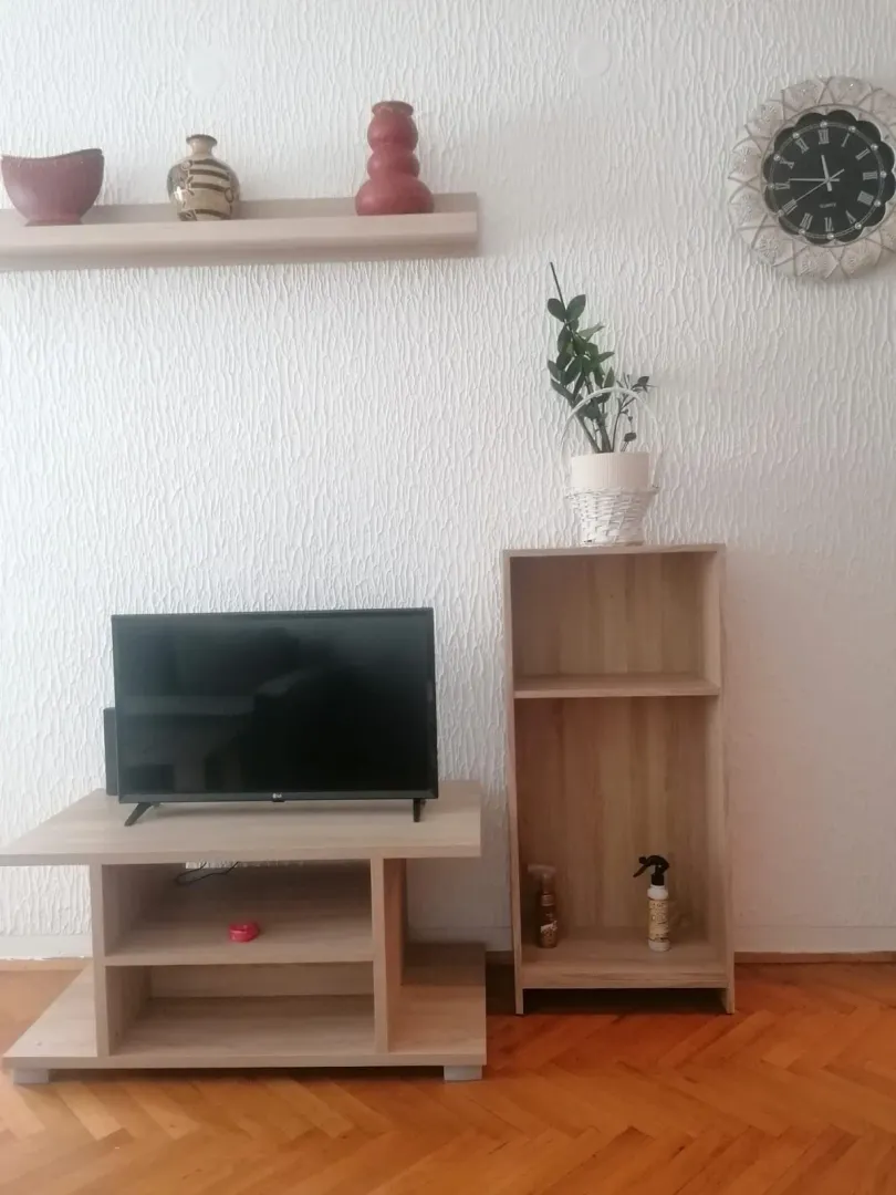 Dnevna soba sa TV komodom, policama i dekorativnim elementima na zidu.