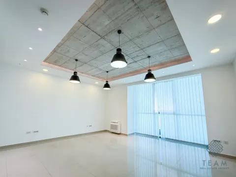 Empty living room with a concrete drop ceiling and pendant lights. - image 9