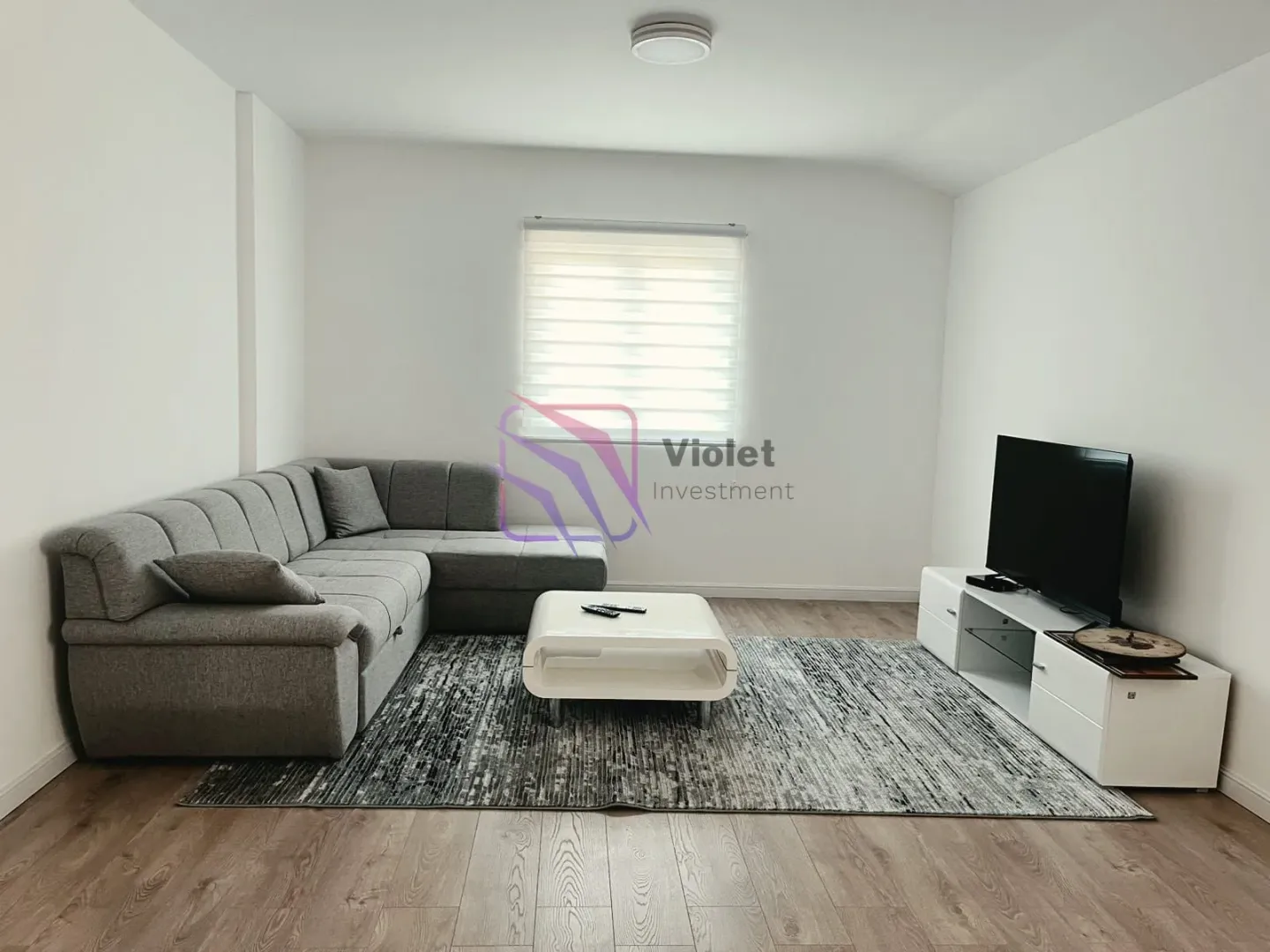 Dnevna soba sa ugaonom garniturom, stočićem i televizorom.