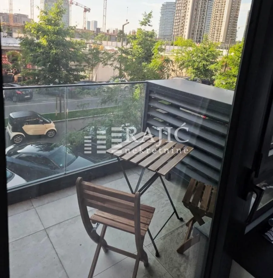 Small furnished balcony with a wooden table and chairs and a city view.