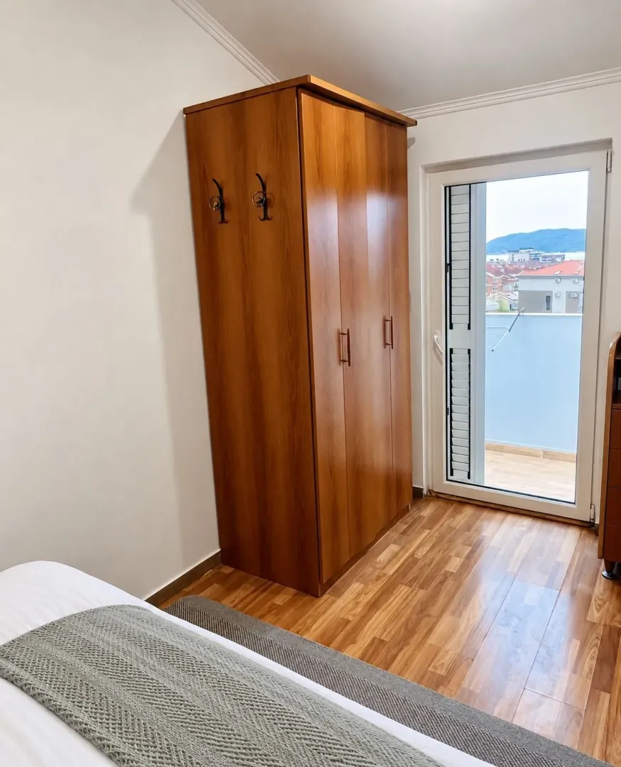 Spavaća soba sa drvenim ormarom i izlazom na terasu.