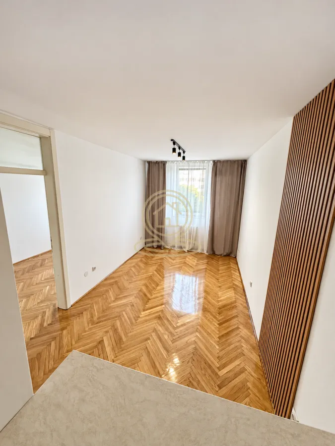 Prazna soba sa parketom i drvenim zidnim panelom.