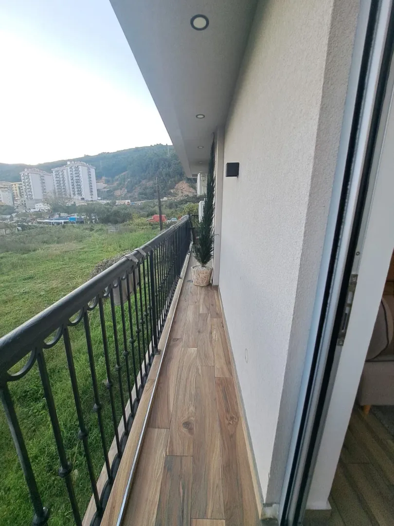 Dugi balkon sa drvenim podom i pogledom na prirodu i grad.