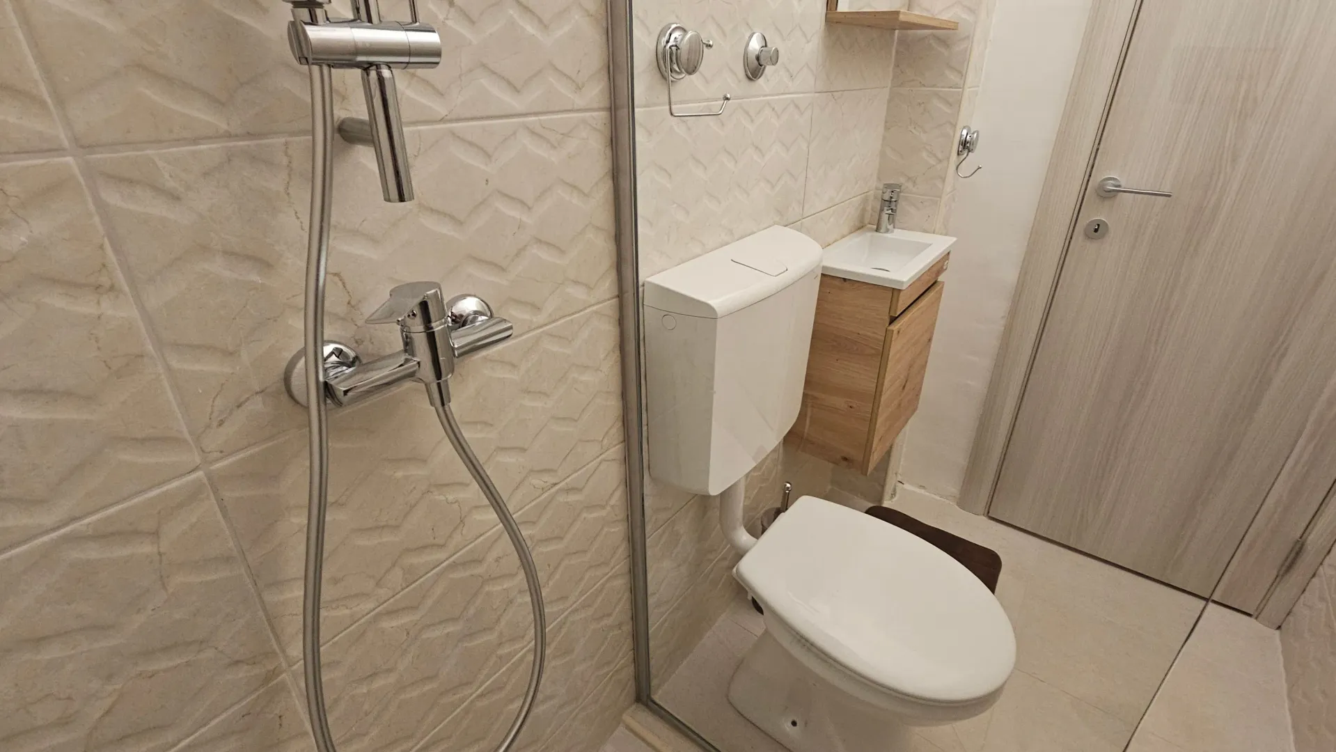 Manje moderno kupatilo sa tuš kabinom, toaletom i malim umivaonikom.