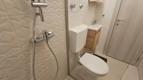 Manje moderno kupatilo sa tuš kabinom, toaletom i malim umivaonikom. - image 7