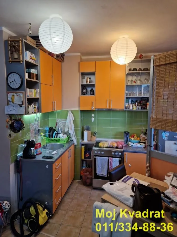 Manja kuhinja sa narandžastim elementima i zelenim zidnim pločicama.