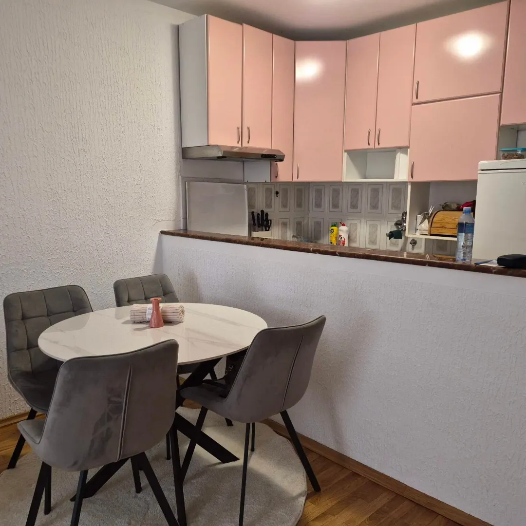 Dining area with a round table and chairs next to a kitchen with pink cabinets.