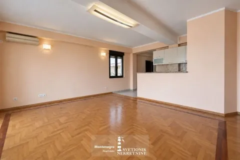 Prostrana dnevna soba sa parketom i kuhinjom u pozadini. - image 3