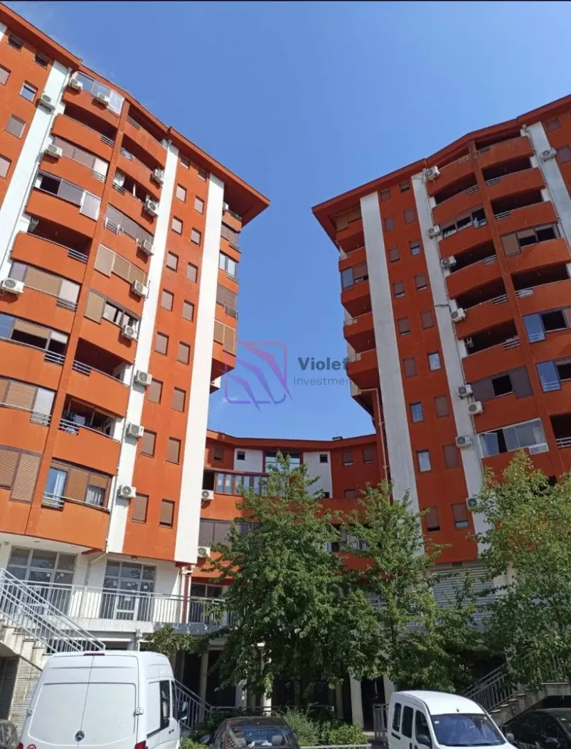 Pogled na spoljašnjost stambene zgrade sa dvorištem i parkiranim vozilima.