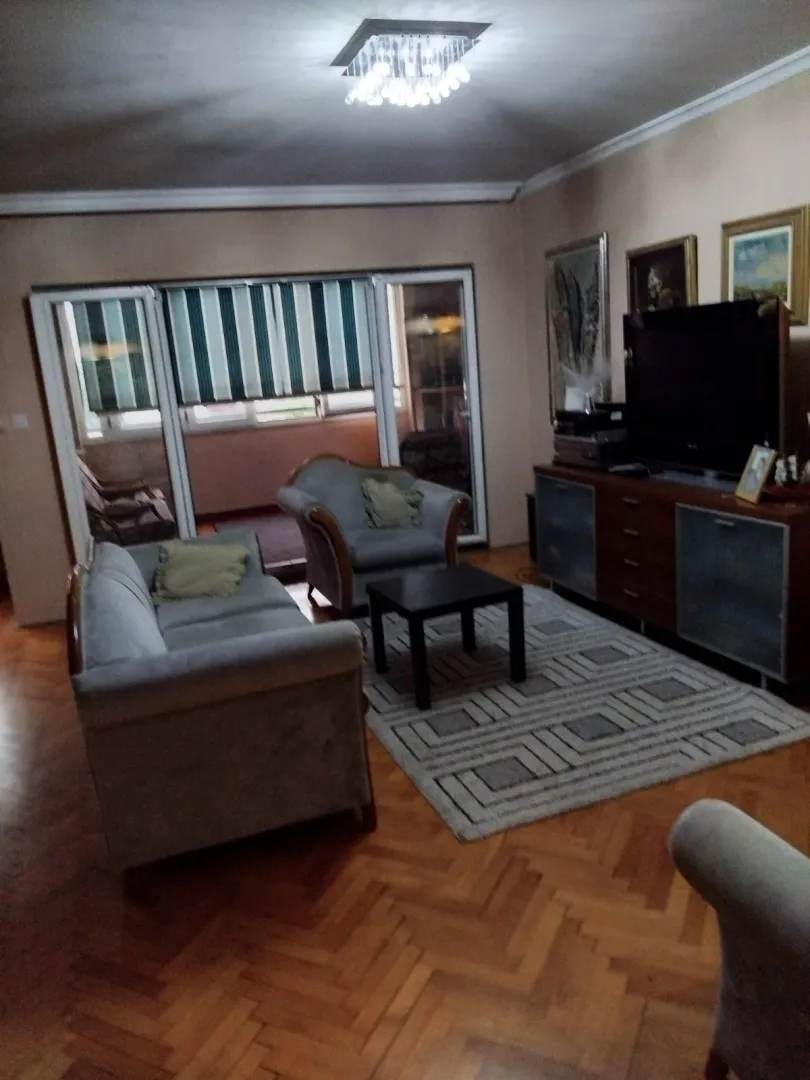 Dnevna soba sa garniturom za sjedenje, drvenom komodom i televizorom.