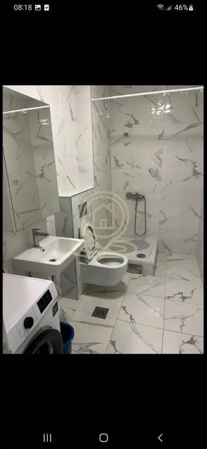 Manje kupatilo obloženo svetlim mermernim pločicama sa umivaonikom, WC šoljom i tuš kabinom.