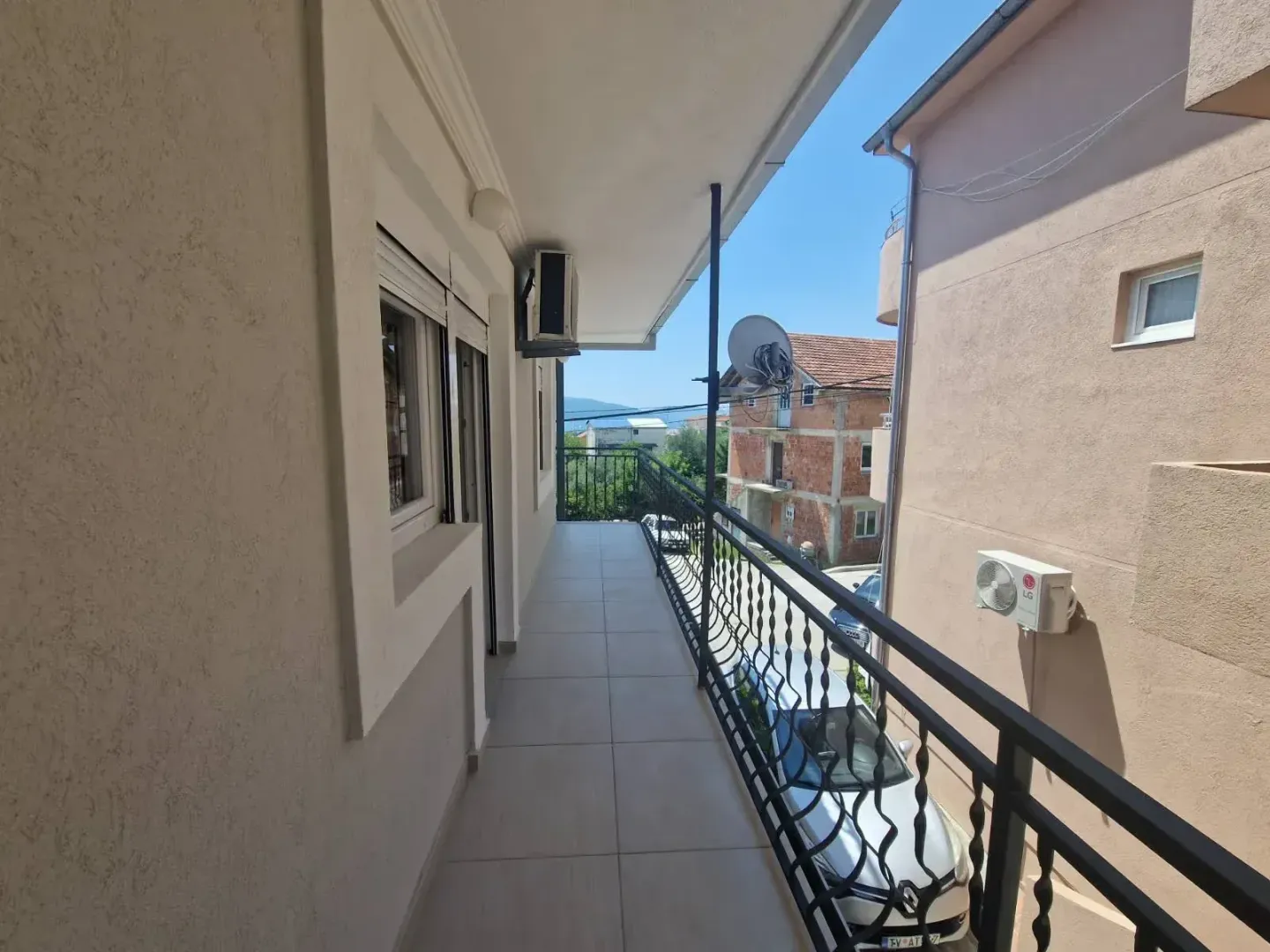 Long tiled balcony with a black railing and a view of surrounding buildings and the street.