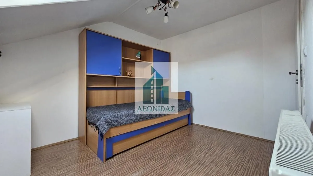 Children's bedroom with a bed and blue built-in wardrobe under a sloped ceiling.