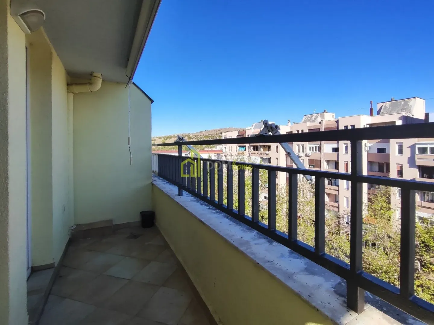 Covered balcony space with a metal railing and a view of surrounding buildings and landscape.