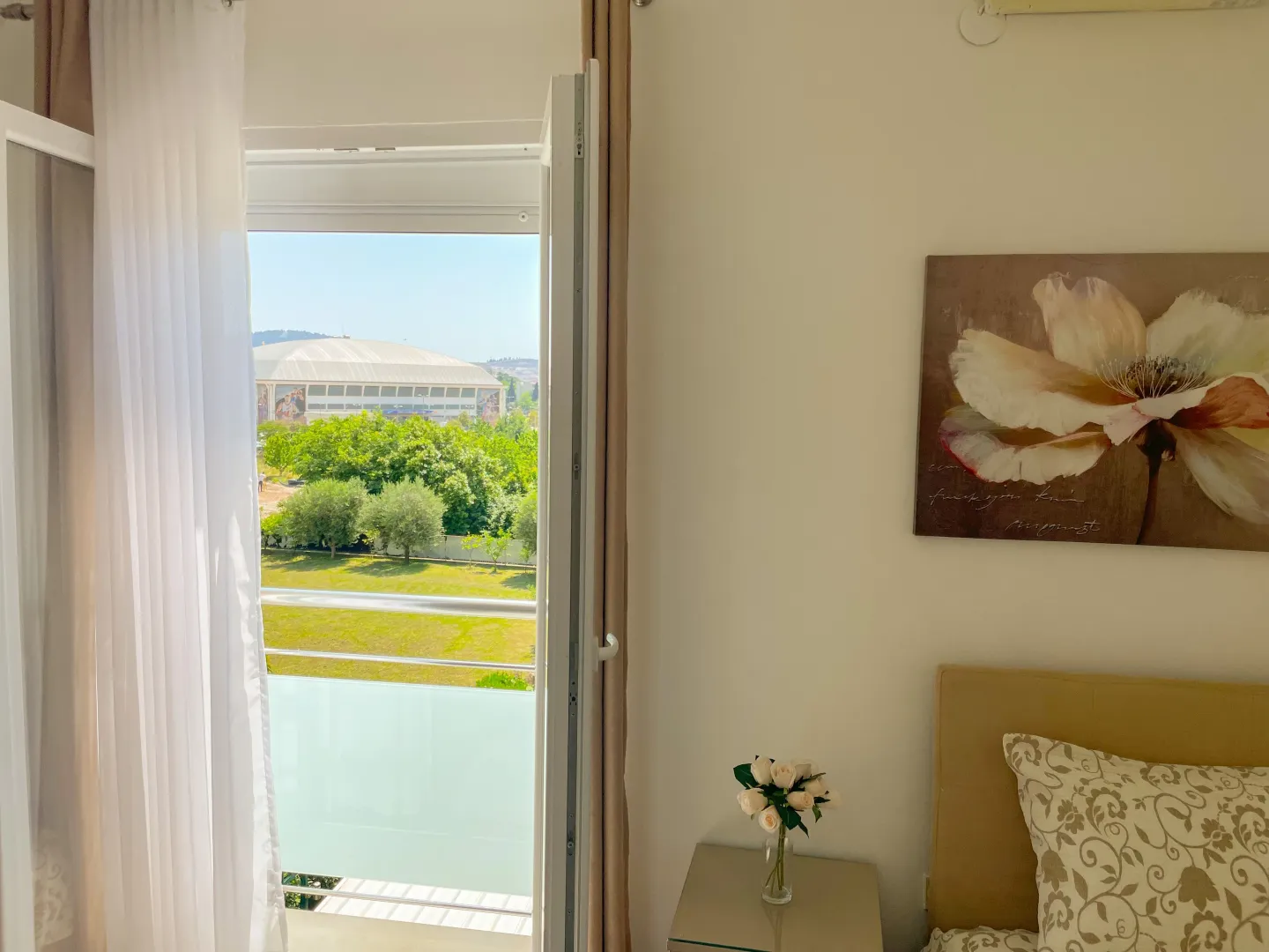 View from the bedroom through the balcony doors towards greenery and surroundings.