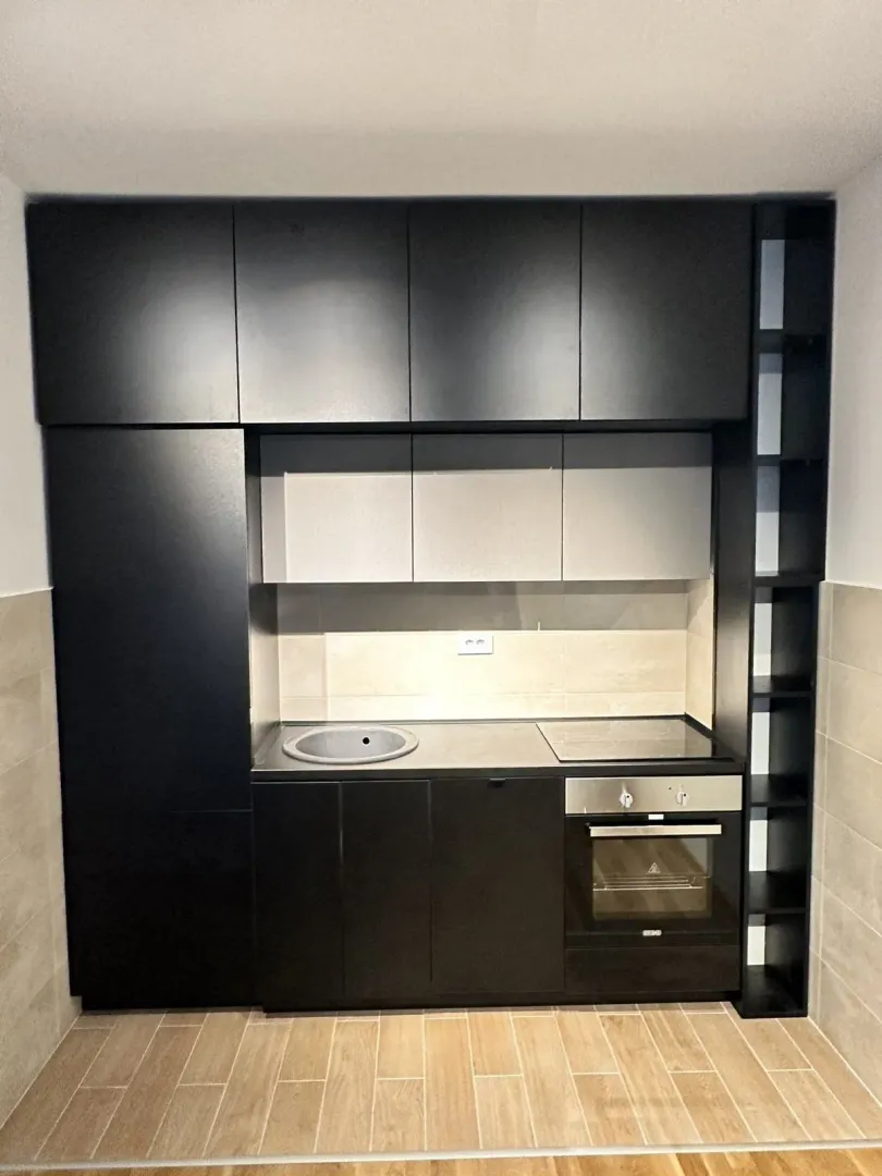 Modern black kitchen with built-in appliances and light tiles.