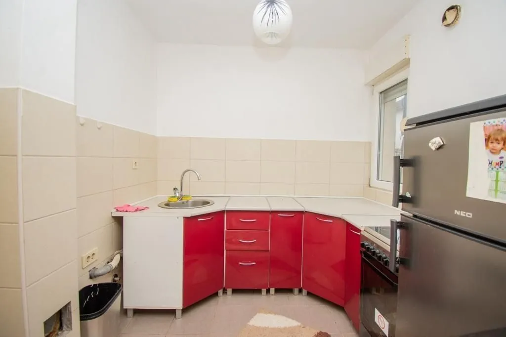 A simple kitchen with red cabinets and a refrigerator.
