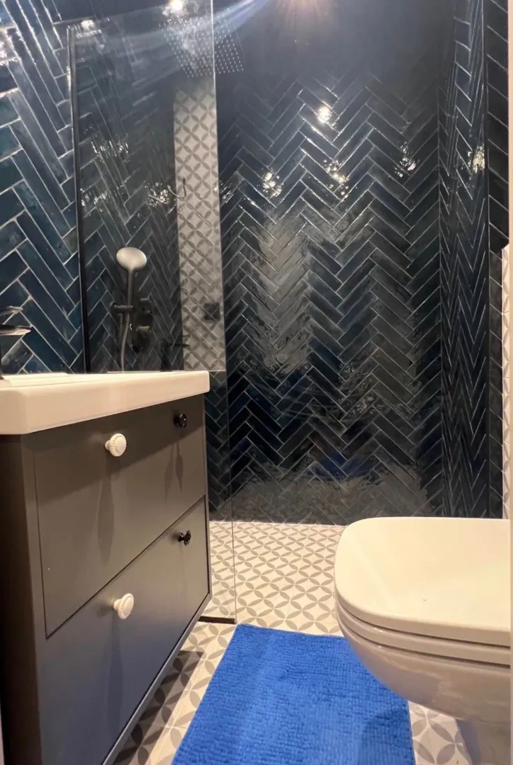 Moderne kupatilo sa tamnoplavim pločicama u ribljoj kosti, umivaonikom i wc šoljom.