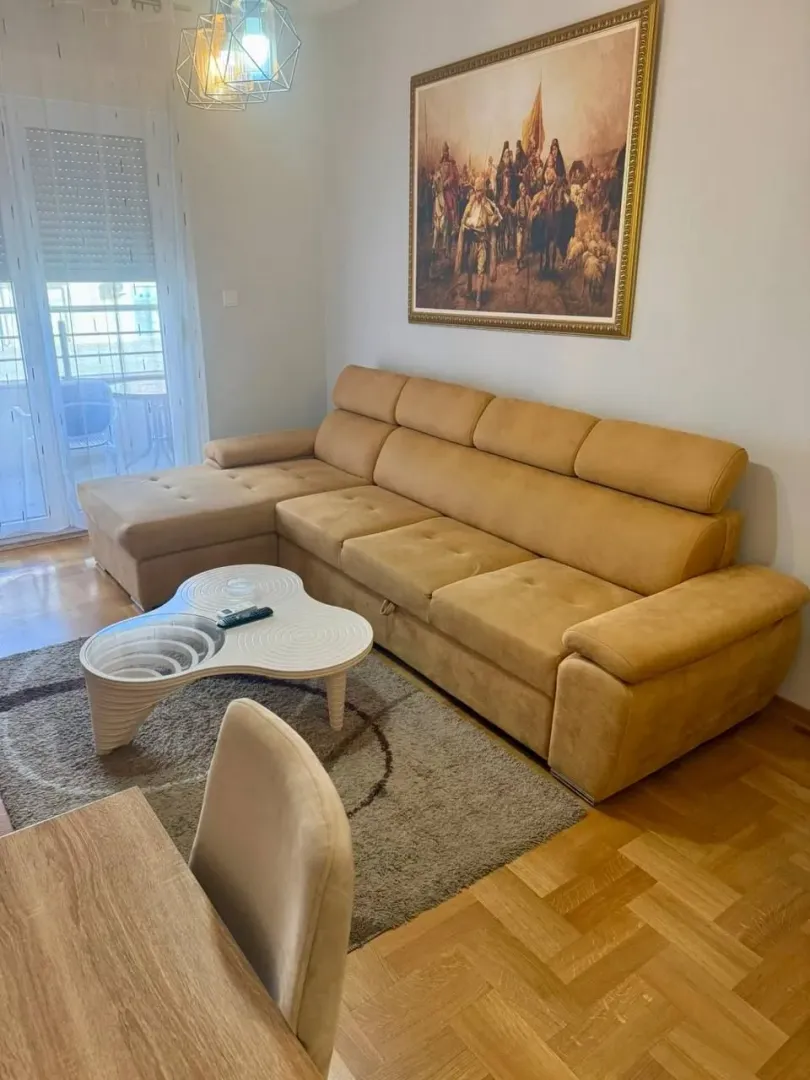 Dnevna soba sa ugaonom garniturom, stočićem i slikom na zidu.