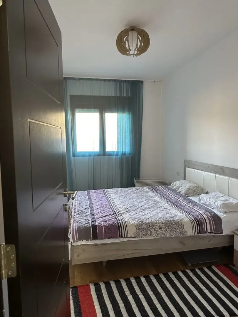 Spavaća soba sa bračnim krevetom, prozorom i pogledom na enterijer.