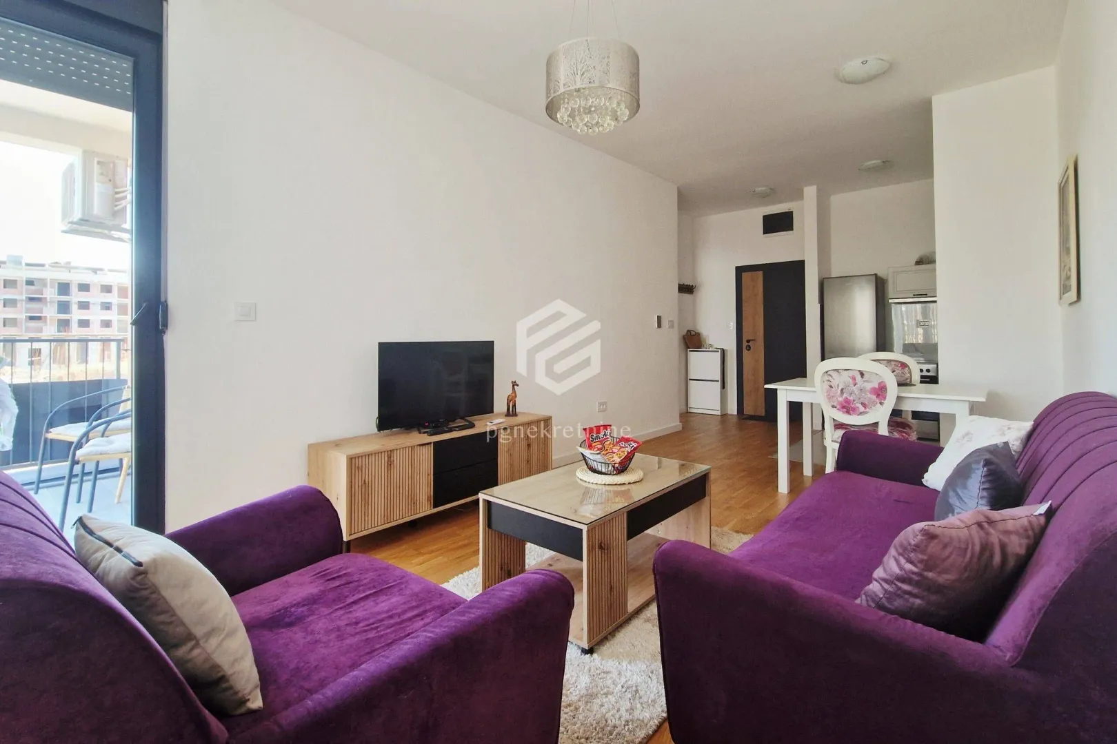 Living room with purple sofas, TV unit, and dining area in the background.