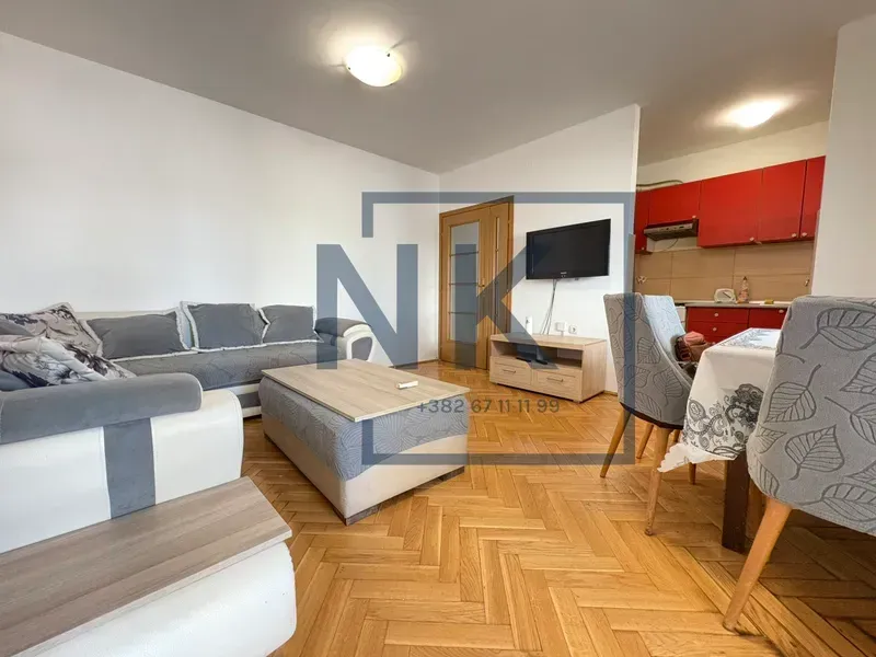 Living room with a sofa, TV, and dining table, connected to the kitchen.