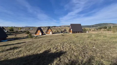 Pogled na drvene vikendice sa prostranim dvorištem i brdima u pozadini. - image 10