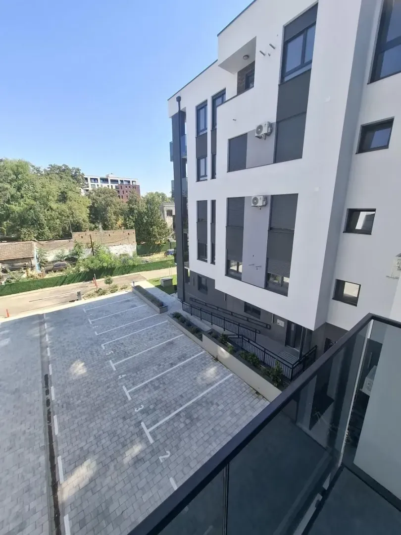 Pogled sa terase na parking prostor i fasadu stambene zgrade.