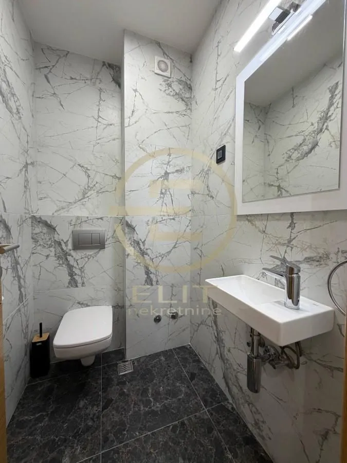 Compact bathroom tiled in marble-patterned tiles with a wall-hung toilet and washbasin.
