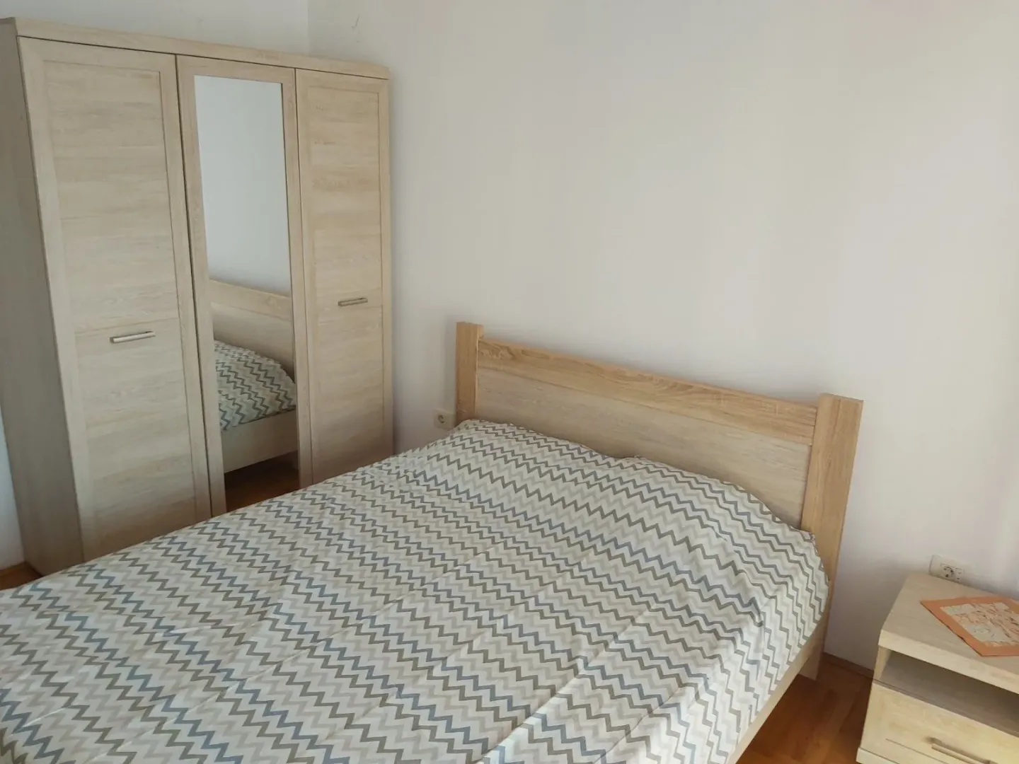 Spavaća soba sa drvenim krevetom, ormarom i noćnim ormarićem.