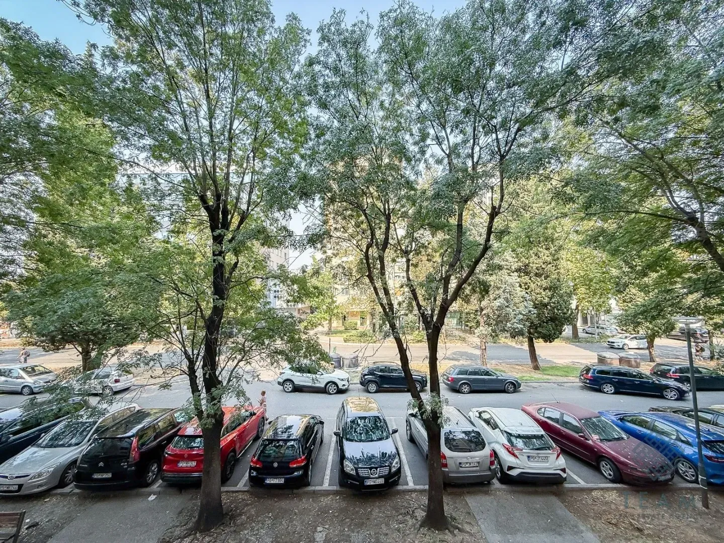 Pogled sa prozora na parking i drveće.