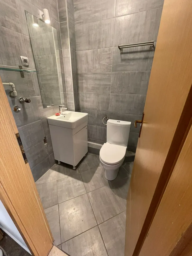 Small bathroom with grey tiles, washbasin and toilet bowl.