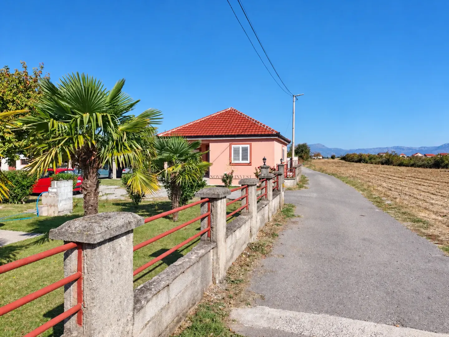 View of the exterior of the house with a yard, fence, and palm trees.