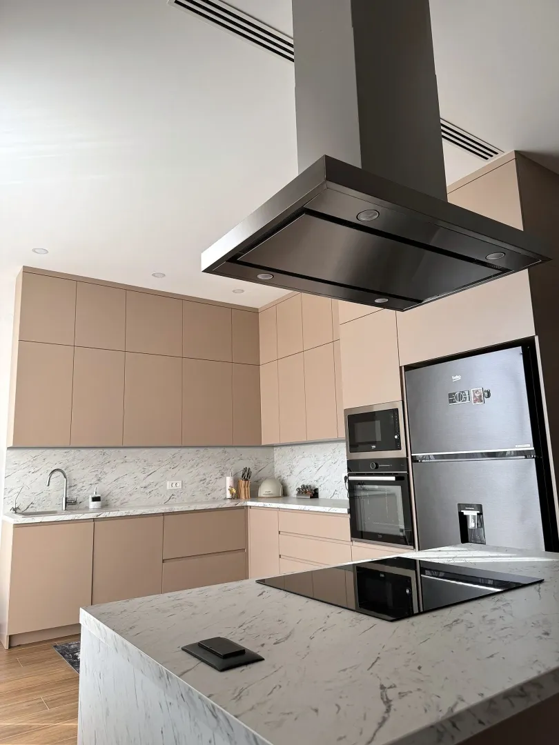 Modern kitchen with beige cabinets, marble countertops, and built-in appliances.