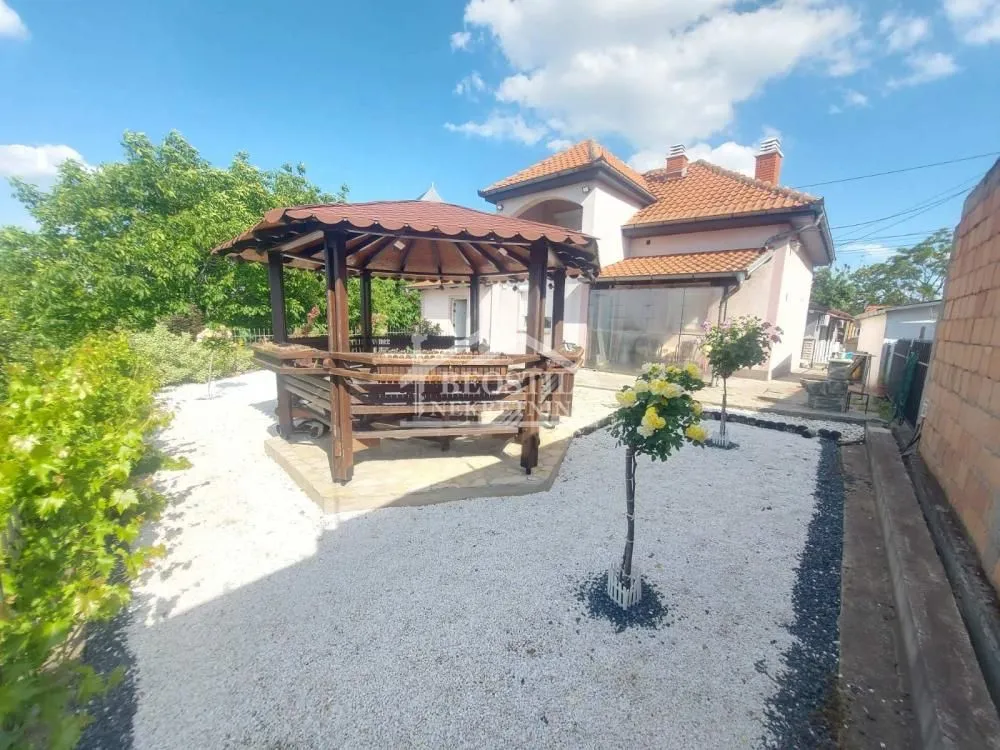 Dvorište kuće sa drvenom letnjikovcem i uređenom baštom.