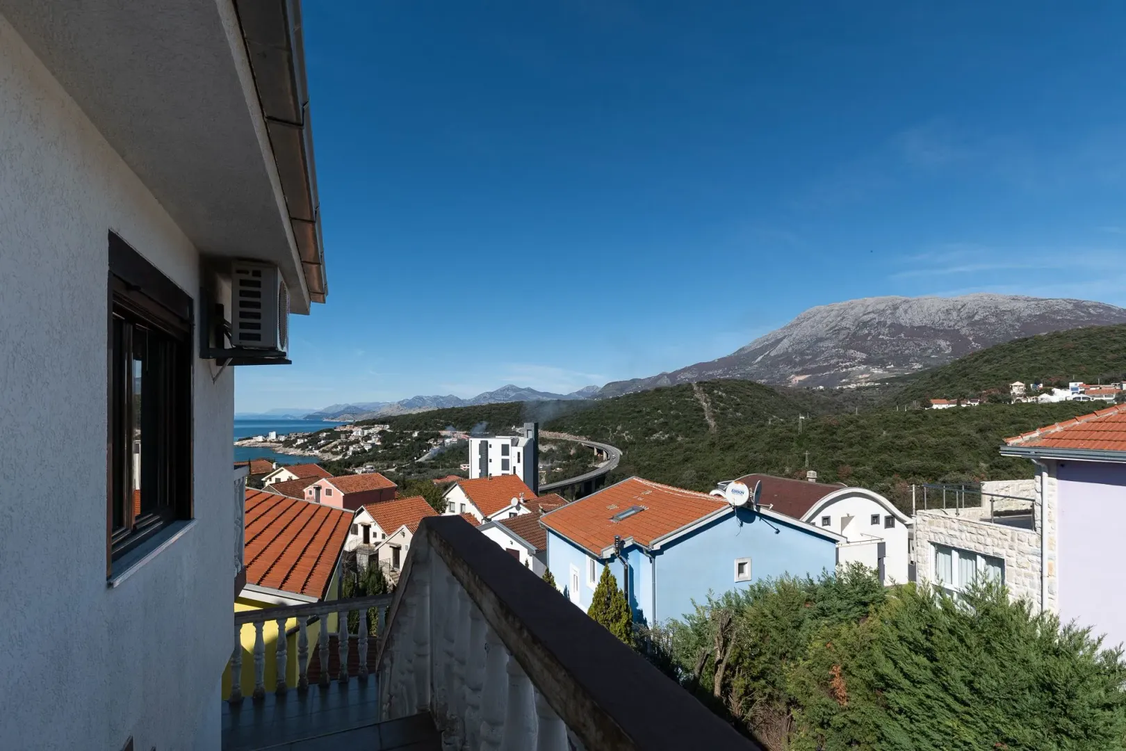 Pogled sa terase kuće na okolno naselje, more i planine.