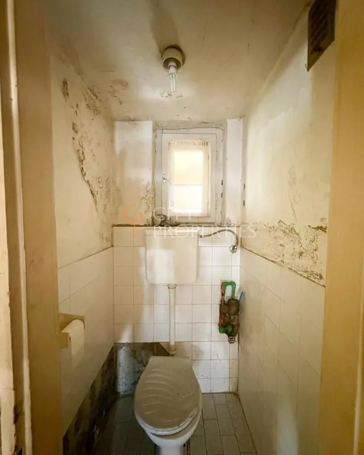 Starije kupatilo sa wc šoljom i zidnim pločicama kojima je potrebno renoviranje.